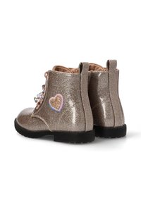 Botas de tobillo beige brillantes con un acabado brillante, parche de corazones rosa y azul, diseño de cordones y suela de goma negra.
