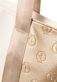Beige leren tote bag met een gouden gestructureerd paneel. Accenten zijn een patroonoppervlak en een brede, gladde schouderriem.