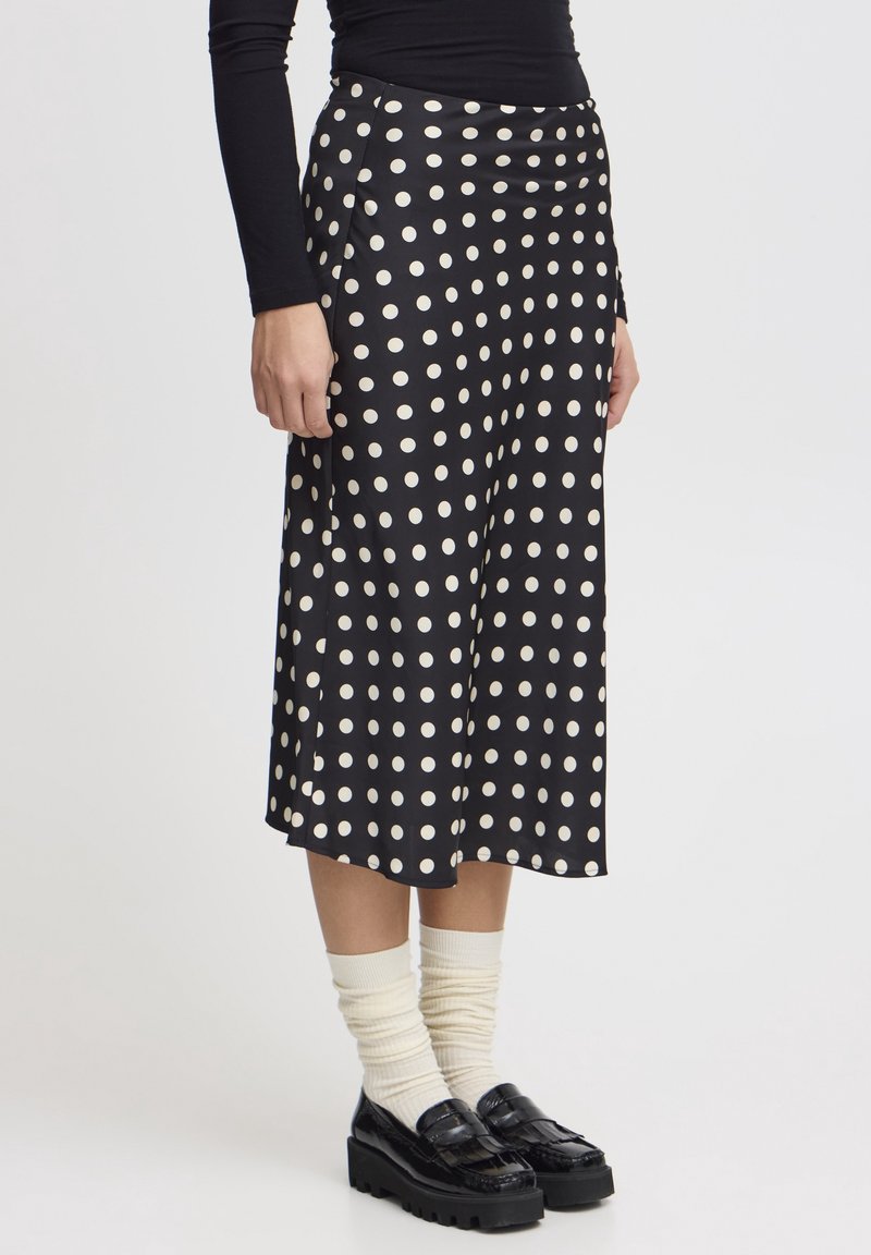 Personne portant une jupe midi noire à pois blancs, des chaussettes crème froissées, des mocassins noirs à plateforme et un haut noir à manches longues.
