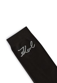 Sort strømpe lavet af glat stof med en ribbet kant. Har et sølv broderet logo "Karl" på siden.