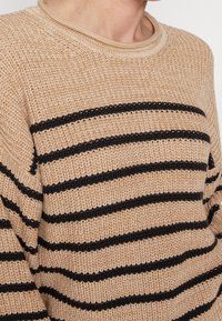 Beżowy sweter dzianinowy w czarne poziome paski, z okrągłym dekoltem i teksturowanym wzorem materiału. Bez dodatkowych ozdób.