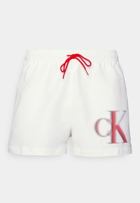 Shorts bianchi con una cintura elastica e un laccio rosso. Presentano un grande logo "ck" rosso e grigio sul lato anteriore sinistro.