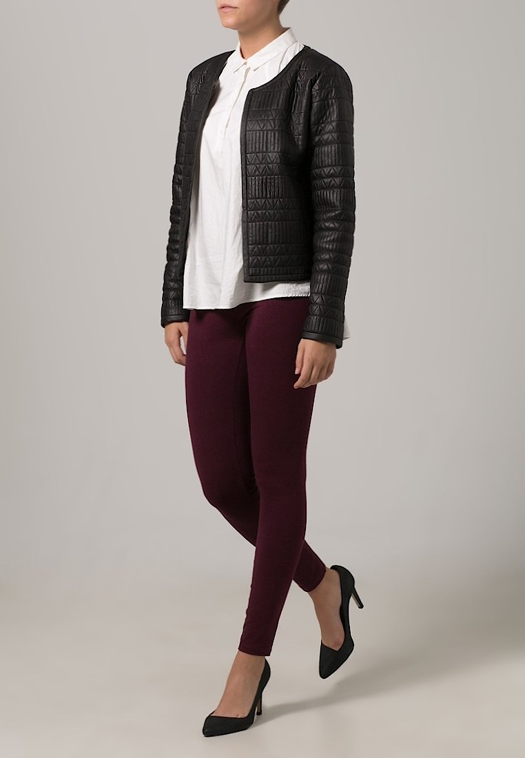 Svart kviltad jacka med ett strukturerat mönster, parat med en vit skjorta med krage och vinröda leggings. Svarta högklackade skor avslutar outfiten.