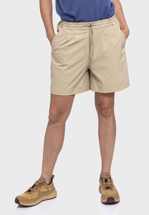 Beige Shorts mit elastischem Bund, Kordelzug, vorderen Falten und Seitentaschen; kombiniert mit braunen Sportschuhen.