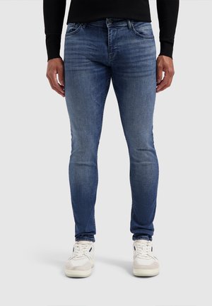 Schmal geschnittene blaue Jeans aus Denim, mit einer ausgewaschenen Optik, fünf Taschen und Gürtelschlaufen, kombiniert mit weißen Sneakers.