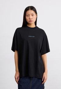 Camiseta de algodón negra con corte holgado, mangas cortas y escote redondo. Presenta bordado frontal en texto azul: "Carhartt, WIP."