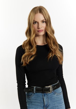 Maglietta nera a maniche lunghe con texture a coste, abbinata a jeans in denim blu a vita alta e una cintura nera con dettagli metallici sulla fibbia.