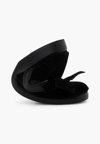 Sandal en terciopelo negro con punta redonda, suela plana de goma y un lazo decorativo en la correa. Textura suave y diseño minimalista.