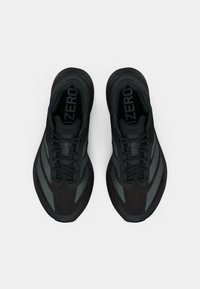 Chaussures de sport noires avec une tige texturée, des accents gris et un bout arrondi. Le design comprend des lacets et une semelle rembourrée.