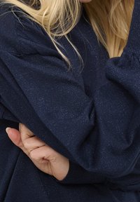 Maglione blu navy con un motivo a maglia testurizzato, caratterizzato da sottili fili metallici, maniche voluminose e polsini a costine.
