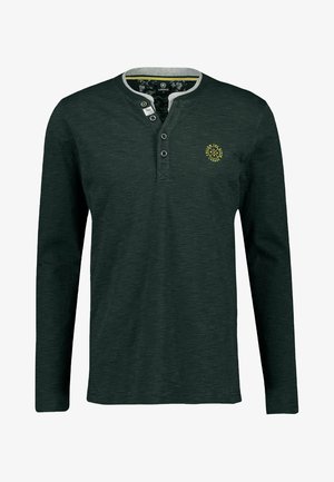 Camiseta henley de manga larga en verde oscuro con tejido texturizado, tapeta con tres botones, ribete gris en el cuello y pequeño logo amarillo en el pecho.
