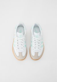 Zapatillas blancas con rayas azul claro y detalles en ante gris. Suela de goma texturizada y cordones clásicos. Diseño minimalista.
