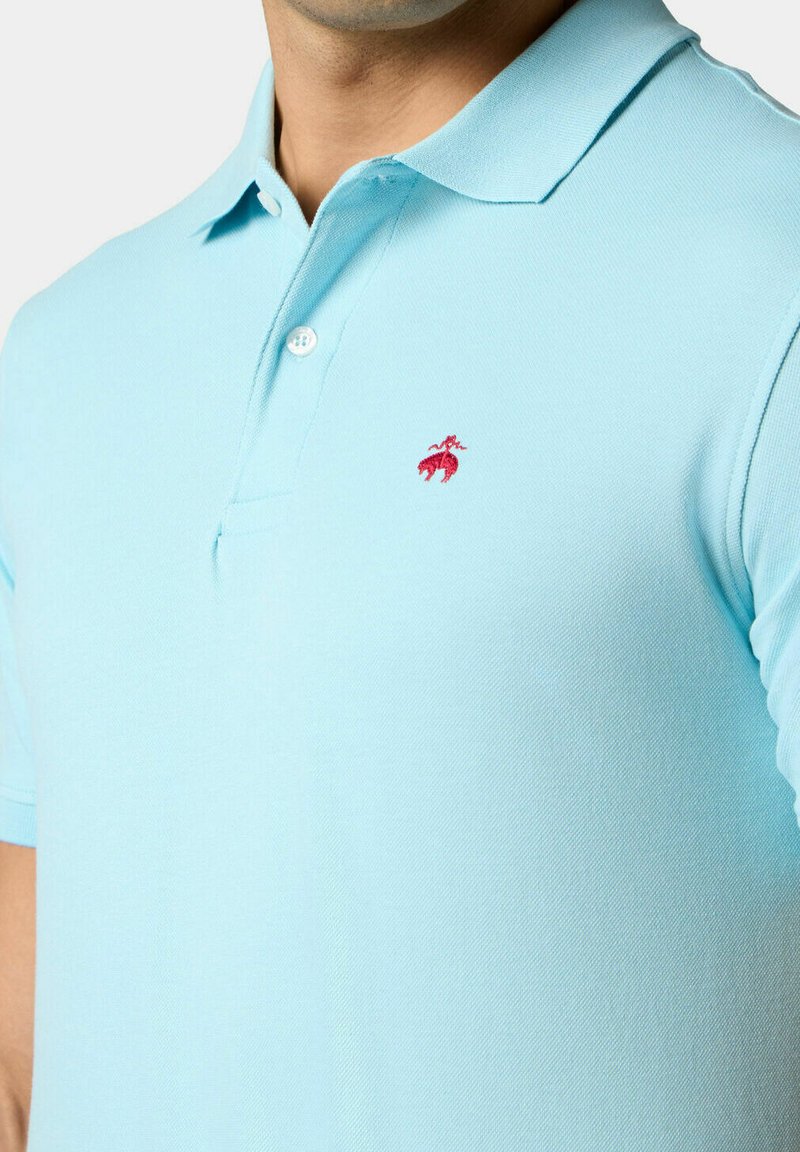 Lichtblauwe poloshirt van gestructureerde stof, met een rood geborduurd logo op de linkerborst en een klassieke kraag met twee knopen.