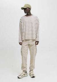 Gestreiftes langärmliges Hemd in Weiß und Beige, kombiniert mit beigen Cargohosen mit Seitentaschen und elastischen Bündchen sowie beigen Sneakern.