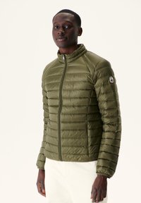 Chaqueta acolchada verde con cuello alto, presenta un cierre de cremallera y textura acolchada horizontal. Parche con logo en la manga izquierda.