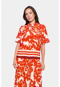 Blusa a maniche corte con motivo rosso e bianco, colletto a fiocco e accentuazione a righe orizzontali vicino all'orlo, realizzata in tessuto leggero.