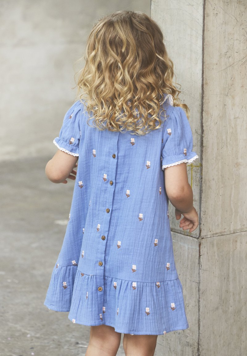 Himmelblaues Baumwollkleid mit kurzen Ärmeln, floralen Stickereien, Knopfverschluss und gerafftem Saum. Mit gewelltem Spitzenrand an den Ärmeln.