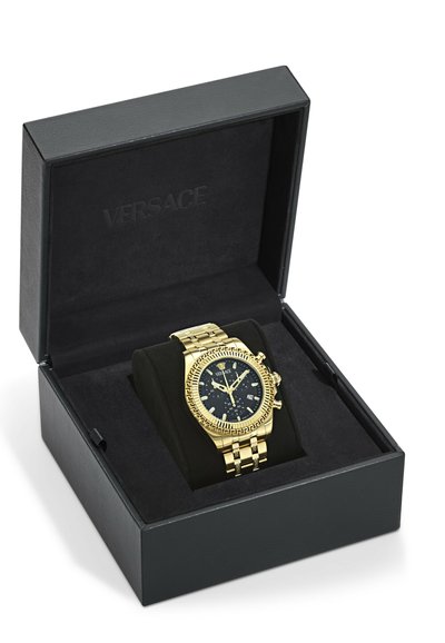 Guld Versace armbåndsur med sort urskive og kronograf, hvilende på en sort pude inde i en åben sort Versace æske.