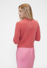 Rozsda színű kötött pulóver kerek nyakkal, hosszú ujjal és bordázott textúrával, sima rózsaszín szoknyával párosítva.