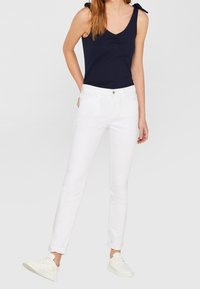 Weiße eng anliegende Jeans mit umgeschlagenen Säumen und einer vorderen Tasche, kombiniert mit einem navyfarbenen Tanktop mit gerafftem Ausschnitt und Schulterschlaufen.
