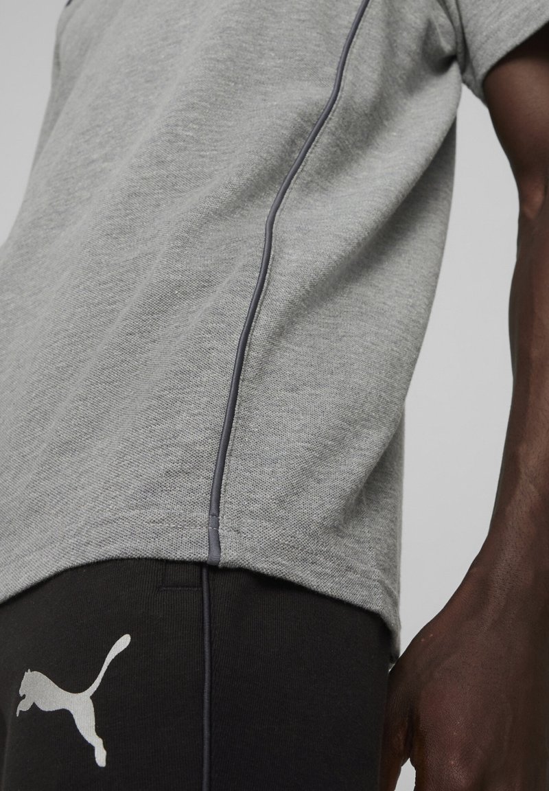 Grijs sport T-shirt met contrasterende donkergrijze stiksels, gecombineerd met zwarte broek met een wit Puma-logo. Focus op de stoftextuur.