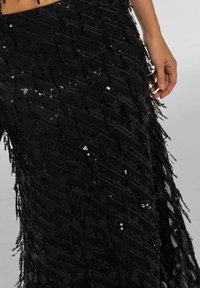 Falda negra con tejido texturizado y lentejuelas en un patrón de cheurón, adornada con flecos a lo largo del dobladillo para un detalle adicional.