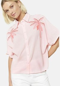 Camicia a maniche corte con bottoni di colore rosa chiaro a righe verticali. Presenta design di palme ricamate in corallo sul davanti.