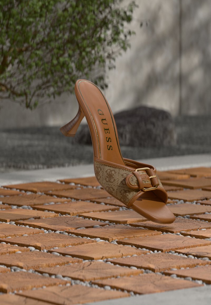 Sandale à talon haut à bout ouvert de la marque Guess en marron avec tissu à motif et détail de boucle, présentée sur une surface extérieure en carreaux de bois.