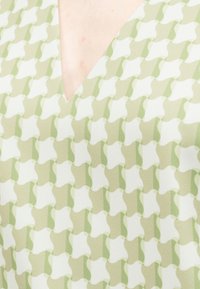 Gros plan d’un tissu à motifs verts et blancs avec un col en V dévoilant une peau pale.