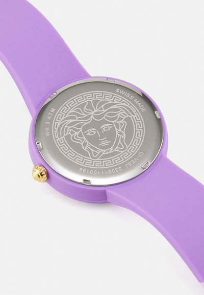 Vijolična silikonska ura s okroglo srebrno številčnico, ki vsebuje podroben dizajn Meduze. Vključuje zlato krono in gravuro "SWISS MADE".