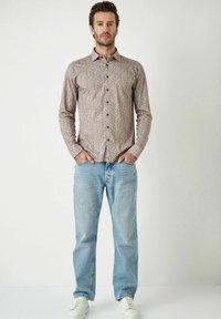 Langarmshirt met een bruin paisleypatroon. Gemaakt van lichte stof, gecombineerd met lichtblauwe jeans en witte sneakers.