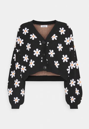 Schwarzer, kurz geschnittener Cardigan mit weißen Gänseblümchenmustern mit orangefarbenen Zentren, V-Ausschnitt, Frontknöpfen und langen, ballonförmigen Ärmeln.