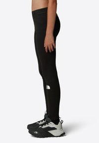 Svarta leggings med hög midja och logotyp på underbenet, tillsammans med svarta och grå träningsskor med en robust sula.