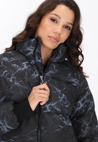 Gevoerde zwarte jas met een gemarmerd patroon in grijs, met een hoge kraag, ritssluiting aan de voorkant en elastische manchetten.