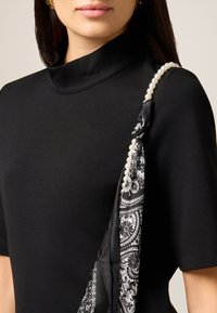 Czarna sukienka o wysokim dekolcie z krótkimi rękawami, z wzorzystym czarno-białym szalem z perłowymi akcentami zarzuconym na ramieniu.
