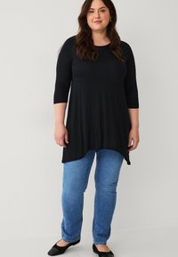 Sort tunika med trekvartærmer og rundet kant, parret med lyseblå lige ben jeans og sorte flade sko. Glat, blød stofstruktur.