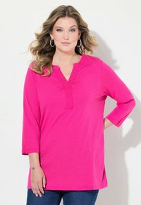 Top fucsia a maniche lunghe con scollo a V e dettagli a costine. Presenta una vestibilità rilassata e spacchi laterali per il comfort. Tessuto morbido e leggero.