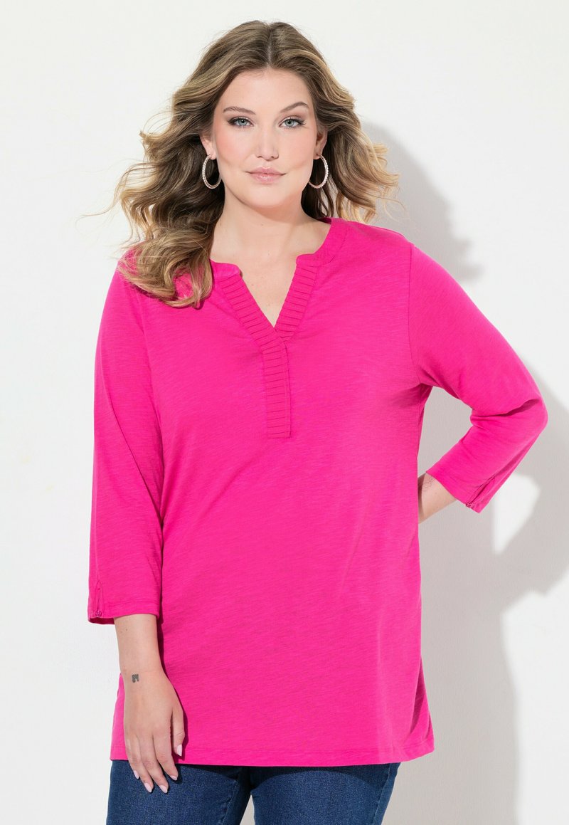 Top fucsia a maniche lunghe con scollo a V e dettagli a costine. Presenta una vestibilità rilassata e spacchi laterali per il comfort. Tessuto morbido e leggero.