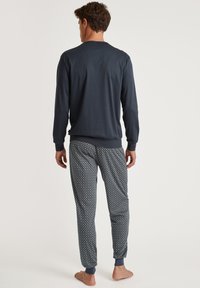 Top navy a maniche lunghe con scollo a V, abbinato a pantaloni da pigiama con un motivo geometrico blu e giallo e polsini elasticizzati.