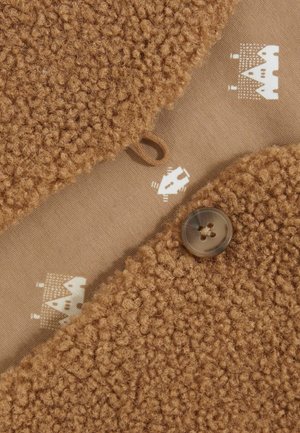 Brunt tekstureret stof med en blød, fnugget overflade og et glat indre lag med et kremfarvet mønster. En rund knap er synlig på kanten.