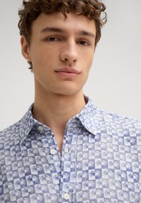Camicetta a maniche corte con bottoni, di colore azzurro chiaro e bianco, caratterizzata da un motivo a granchio, colletto e bottoni decorativi. Tessuto leggero.