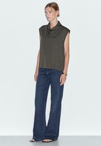 Oliwkowy bezrękawnik o dekolcie typu cowl, zestawiony z ciemnoniebieskimi spodniami z szerokimi nogawkami. Gładki materiał o luźnym kroju.