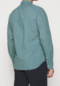 Grün und marineblau kariertes Hemd mit langen Ärmeln. Verfügt über einen Button-Down-Kragen, einen abgerundeten Saum und geknöpfte Manschetten mit kontrastierenden Beschlägen.