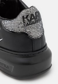 Baskets noires avec un dessus en cuir texturé et un accent en maille étincelante au niveau du talon. Logo "KARL LAGERFELD" affiché de manière proéminente à l'arrière.