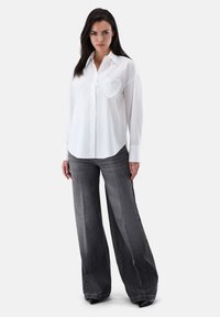 White button-up shirt with a ruffled heart appliqué on the chest. Paired with wide-leg, gray denim pants featuring a faded texture.