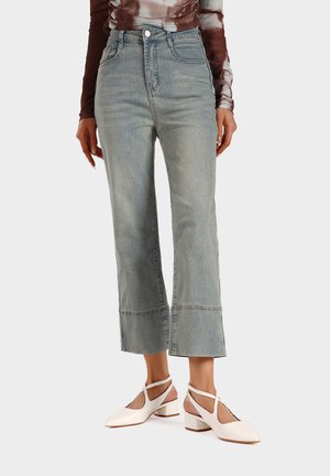 Jeans azzurri chiari a vita alta con gamba dritta, lavaggio sbiadito e orlo grezzo. Abbinati a scarpe bianche con tacco a blocco e design con ritagli.