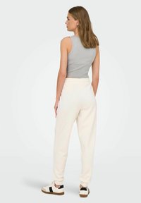 Grå ærmeløs crop top kombineret med cremede sweatpants. Outfitten har en blød tekstur og afslappet pasform, med sorte detaljer på skoene.