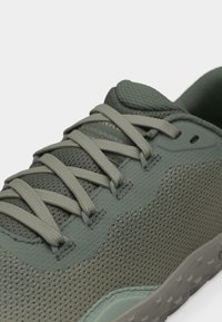 Πράσινο αθλητικό παπούτσι από δίχτυ και συνθετικό υλικό με κορδόνια στο ίδιο χρώμα, επενδυμένη γλώσσα και υφή στη σόλα, απεικονισμένο σε κοντινή γωνία.