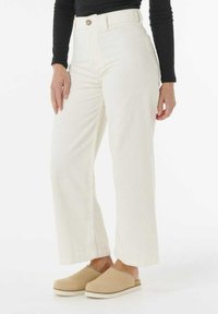 Bredde ben af corduroy i off-white, med høj talje, frontknap og struktureret stof. Parret med lysebeige slip-on sko.
