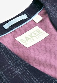 Mornarska obleka z blagim leskom, ki ima svetlo modro oznako in teksturirano rožnato notranjost z ponovljenimi logotipi. Na etiketi piše "BAKER by Ted Baker."